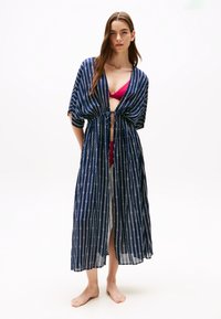 Prozirni mornarski kimono s bijelim vertikalnim prugama, s vezanjem u struku, širokim rukavima i dugim, lepršavim dizajnom, uparen s ružičastim bikinijem.