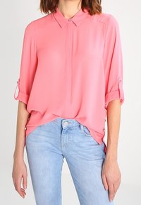 Rosa, lätt blus med krage, uppvikta ärmar och lös passform. Matchat med ljusblå denimjeans.