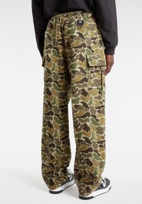 Camouflage cargobroek in groen, bruin en tan, met een elastische tailleband, zijzakken en een ruime pasvorm. Zwarte schoenen maken de look compleet.