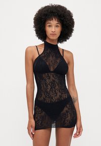 Vestido mini em renda preta com gola alta, alças finas e padrões florais, com uma silhueta ajustada e textura transparente.