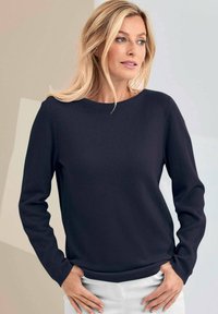 Marineblauer Strickpullover mit langen Ärmeln und rundem Ausschnitt. Glatte Textur und gerippte Bündchen, getragen über weißen Hosen.