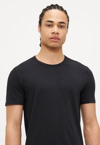 Schwarzes kurzärmliges T-Shirt aus glattem Baumwollstoff, mit rundem Halsausschnitt und figurbetonter Silhouette, ausgestattet mit minimalen Nahtdetails.