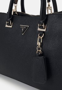 Sort tekstureret læderhåndtaske med guldfarvet hardware, trekantet logo og aftagelig mærkat. Har dobbelte håndtag og lynlåslukning.