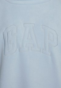 Hellblaues Fleece-Sweatshirt mit erhabenem "GAP"-Schriftzug auf der Vorderseite. Glatte Textur mit Rundhalsausschnitt und lässigem Design.