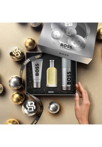 Geur cadeau set met zilveren doos en zwarte binnenkant, bevat een gele fles, twee grijze tubes en een zwarte strik met gouden accenten.