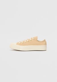 Beige canvas sneakers med vit gummisula, rund tå, snörningsdesign och gyllene ögla. Minimalistisk stil med diskret sömdetalj.