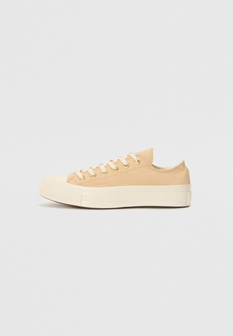 Beige canvas sneakers med vit gummisula, rund tå, snörningsdesign och gyllene ögla. Minimalistisk stil med diskret sömdetalj.