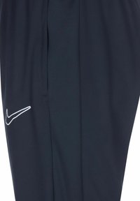 Pantaloni sportivi navy con un pannello laterale texturizzato e il logo Nike swoosh bianco. Presentano una vita elastica e tasche laterali.