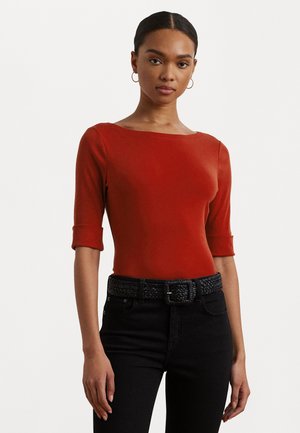 Top rosso aderente con scollatura rotonda e maniche a tre quarti, abbinato a jeans di denim neri e una cintura intrecciata nera.