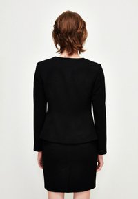 Černý dobře padnoucí oblek s přiléhavým sakem s dlouhými rukávy a peplum spodním lemem, doplněný sukní typu tužka do kolen. Hladká textura.