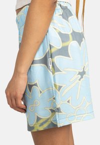 Shorts bleu clair avec de grands motifs floraux en blanc et gris, dotés d'une taille élastique confortable et d'une petite étiquette de marque sur le côté.