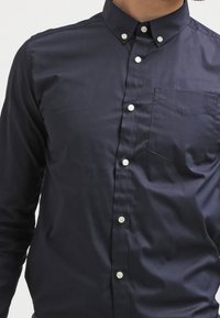 Námořnická košile na knoflíky vyrobená z bavlny s hladkou texturou, se záplatovou kapsou a bílými knoflíky na klasickém límci.