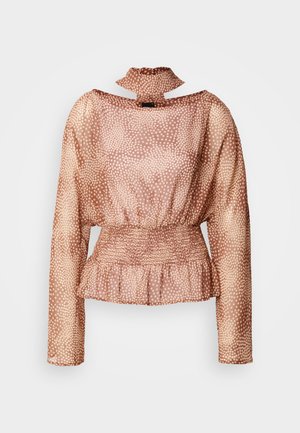 Ανοιχτό καφέ μπλούζα με μακριά μανίκια, λευκές πουά, δέσιμο λαιμού, σφηκοφωλιά στη μέση και βολάν στο τελείωμα σε λευκό φόντο.