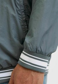 Szara, lekka kurtka z elastycznymi mankietami. Mankiety mają paskowany wzór w białym i szarym kolorze. Materiał ma miękką, gładką fakturę.