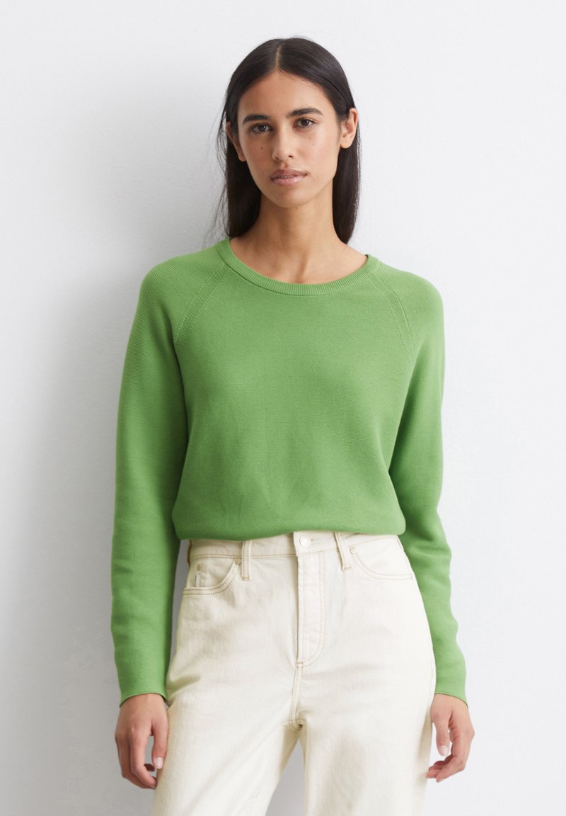 Pull à col rond vert avec tricot texturé, col côtelé et manches longues, associé à un jean blanc taille haute.