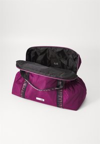 Lilla nylon duffelbag med svarte detaljer, glidelås lukking og doble stoffhåndtak. Innvendig er den svart med en liten logomerking.