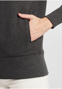 Tmavo sivý sweatshir s rebrovanou textúrou, s bočnou kapsou a rebrovanými manžetami. Bezšvový dizajn s minimálnymi detailmi.