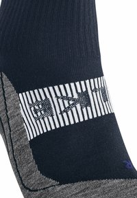 Calcetín negro y gris con textura acanalada. Presenta una banda blanca con rayas y acentos gráficos en negro. Áreas de talón y puntera reforzadas.