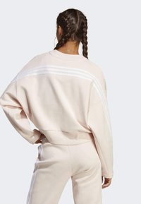 Ljust rosa, oversized sweatshirt med tre vita ränder längs axlarna på baksidan, mjukt tyg, ribbade muddarna och midjan.