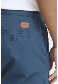 Navy blue shorts with a smooth texture, featuring a back pocket with a button and a brown leather label reading "BLEND."