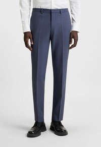 Pantaloni blu slim fit, su misura, con un sottile motivo testurizzato e pieghe pressate, abbinati a scarpe nere. Tessuto liscio e linee pulite.