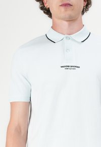 Muž v svetlomodrej polokošeli s čiernym lemom na golieri a čiernym textom „WEEKEND OFFENDER ADMIT NOTHING“ na hrudi.