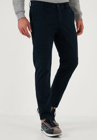 Marineblauwe chino's van een katoenmix, slim fit met voorkeurszakken, riemlussen en subtiele stiksels, gecombineerd met grijze sneakers.