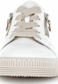 Baskets en cuir blanc avec des lacets beiges, dotées de zips sur les côtés et d'une semelle en caoutchouc texturé avec des rainures horizontales. Design simple et moderne.