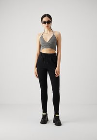 Svart-hvitt rutete kort halterneck topp kombinert med svart tettsittende bukser og kraftige svarte sneakers med gule detaljer.
