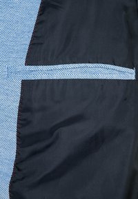 Niebiesko-czarna tkanina w kratkę. Posiada wyraźny szew oraz detal w postaci czerwonego przeszycia na brzegach. Zawiera wewnętrzną kieszeń.