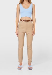 Beżowe spodnie z wysokim stanem, z pętlami na pasek i brązowym paskiem. Jasnoniebieski top zakończony na wysokości talii oraz niebieskie klapki z detalem w postaci węzła. Gładka tekstura.