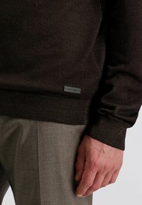 Brauner Strickpullover mit strukturiertem Finish und gerippten Bündchen, versehen mit einem silbernen Etikett mit der Aufschrift "Pierre Cardin" am Saum.