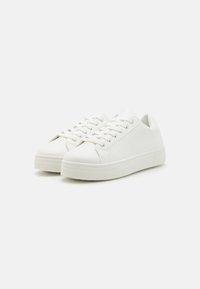 Baskets en cuir blanc à profil bas, à bout rond et semelle en caoutchouc plate. Dispose d'un système de laçage et d'un design lisse et minimaliste.