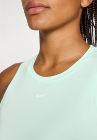 Close-up van de nek en schouder van een vrouw in een mintgroen sporttop, met een klein wit Nike-logo op de borst.