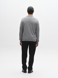 Grijze sweatshirt met een ronde hals, zwarte broek en een grijze pet. De stof lijkt zacht, met minimale stikdetails, gezien vanaf de achterkant.