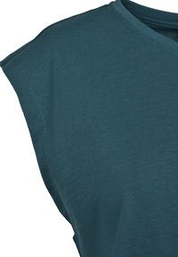 Turkos bomullslös topp utan ärmar med rund halsringning, avslappnad passform och något sänkta axelsömmar. Slät textur med minimala sömnadsdetaljer.