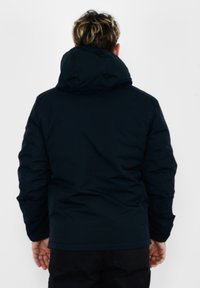 Giacca imbottita di colore blu scuro, dotata di cappuccio e design trapuntato. Il tessuto appare liscio con una finitura opaca, senza loghi o minuterie visibili.