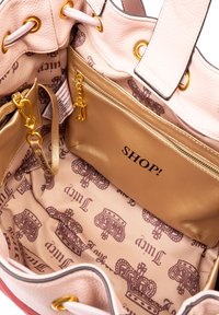 Borsa a mano in pelle beige con hardware dorato. L'interno presenta una fodera beige chiaro con un motivo a corona, una tasca con zip e un dettaglio impresso "SHOP!".