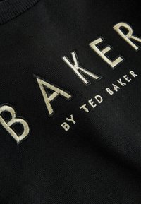 Maglione nero in maglia con grande scritta ricamata "BAKER" color crema e la dicitura più piccola "by TED BAKER", che evidenzia un tessuto strutturato.