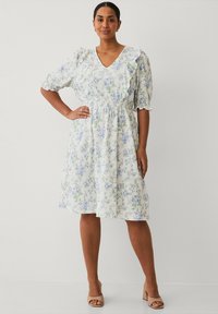Robe en imprimé floral blanche avec des fleurs bleues et vertes. Présente un décolleté en V, des manches bouffantes avec des volants, et une taille élastique pour un ajustement parfait.