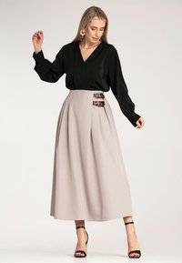 Czarna bluzka z dekoltem w serek i długimi rękawami, w zestawieniu z beżową spódnicą o wysokim stanie z bocznymi klamrami. Całość dopełniają czarne sandały na obcasie.