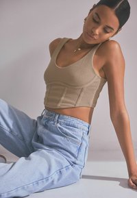 Bež ribikujaga crop top avatud kaeluse ja sanga stiilis rihmadega, koos helesiniste kõrge vöökohaga teksadega juhuslikus poosis.