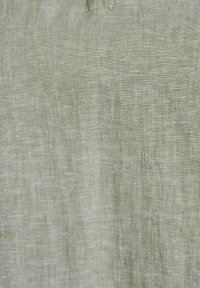 Textúra svetlozelenej ľanovej látky zobrazujúca prirodzený vzor tkania a jemné stehovanie v hornej strede.