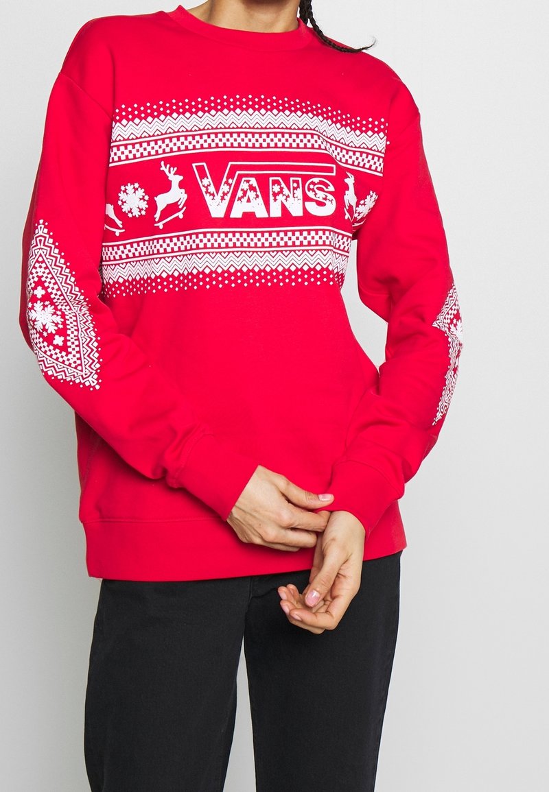 Sudadera roja con acentos blancos estampados, incluyendo renos y copos de nieve, que presenta un logotipo central de "VANS". Mangas largas con puños acanalados.