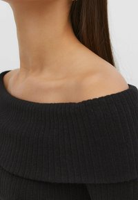 Svart ribbad av-shoulder topp med bred halsringning och texturväv, som från sidan framhäver mjuka konturer vid nyckelbenet och axelområdet.