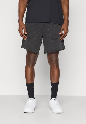 Sorte denim shorts med en frynset kant, som har to frontlommer og syninger. Sammen med hvide sneakers og sorte ankelstrømper.