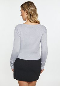 Grå strikket bluse med lange �ærmer og lav ryg, parret med en sort tætsiddende nederdel. Stoffet ser blødt ud med en let tekstur.