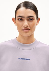 Lichtlila sweatshirt van zacht materiaal, met een ronde halslijn en een blauwe "ARMEDANGELS" logo centraal op de borst.