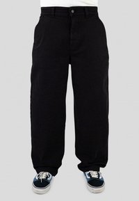 Black denim pants with a loose fit, featuring a front button closure and side pockets. Paired with blue and black sneakers.