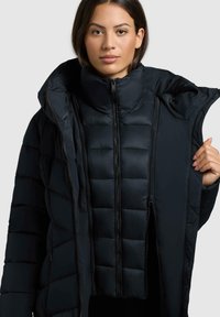Schwarze Pufferjacke mit hohem Kragen, durchgehendem Reißverschluss und gestepptem Muster. Abnehmbare Innenschicht mit vertikalen Nähten und glattem Material.
